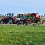 Soil Preparation - a red tractor pulling a trailer of hay through a field