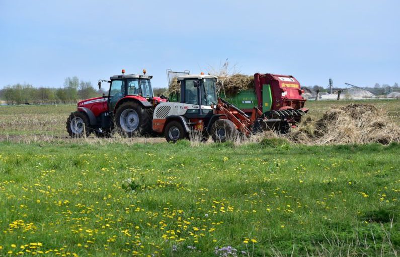 Soil Preparation - a red tractor pulling a trailer of hay through a field