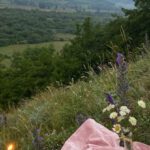 Wildflower Meadow - Pink covering with with candles and wildflowers placed on grassy slope of hill in nature with mountains in distance on summer