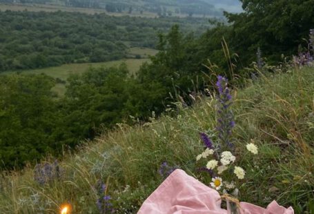 Wildflower Meadow - Pink covering with with candles and wildflowers placed on grassy slope of hill in nature with mountains in distance on summer