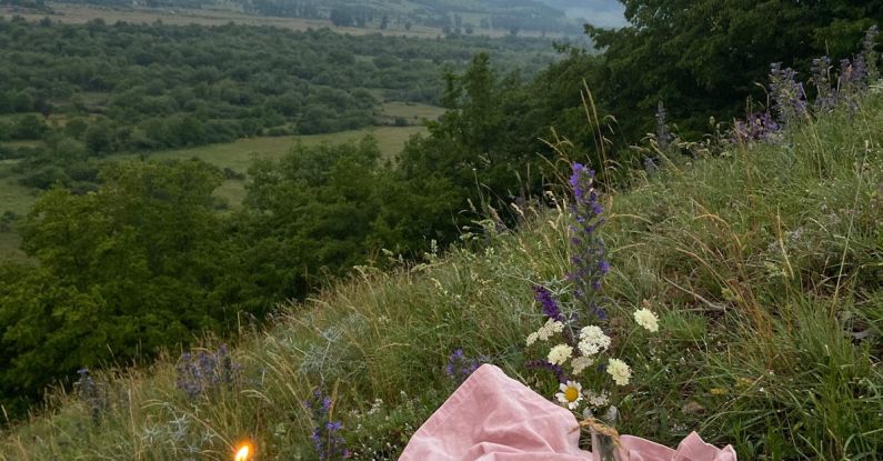 Wildflower Meadow - Pink covering with with candles and wildflowers placed on grassy slope of hill in nature with mountains in distance on summer