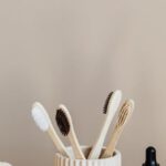 Organic Alternatives - Collection of bamboo toothbrushes and organic natural soaps with wooden body brush arranged with recyclable glass bottle with natural oil and ceramic vase with artificial plant