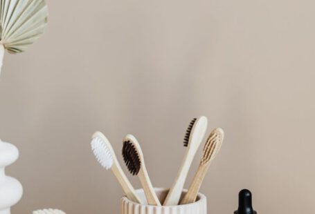 Organic Alternatives - Collection of bamboo toothbrushes and organic natural soaps with wooden body brush arranged with recyclable glass bottle with natural oil and ceramic vase with artificial plant