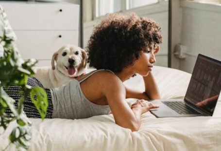 Companion Planting - Relaxed black woman watching laptop near dog on bed