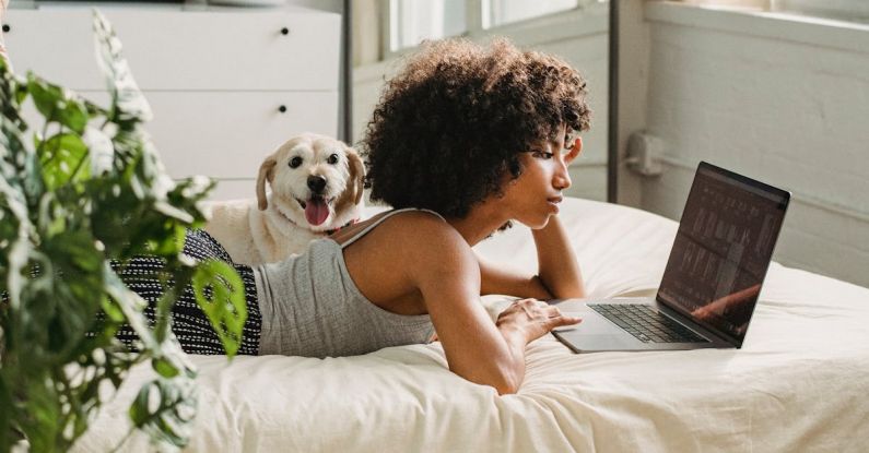 Companion Planting - Relaxed black woman watching laptop near dog on bed